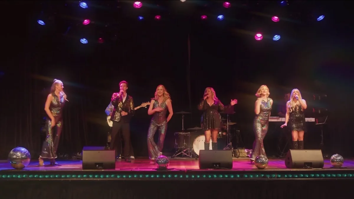 Full cast performing on stage under a row of disco balls