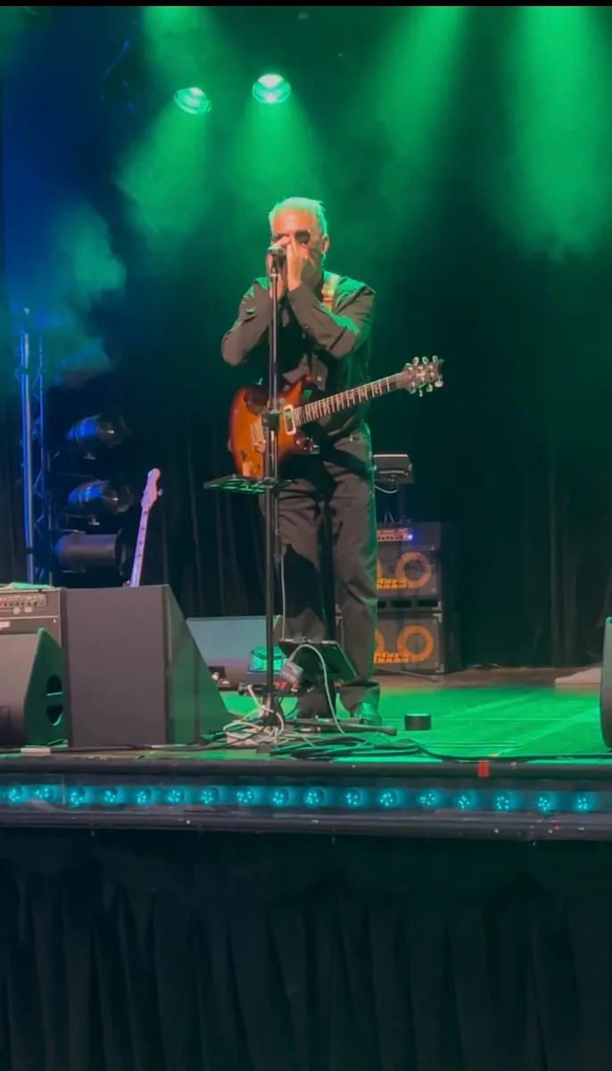 Guitarist in sunglasses singing into a microphone under green stage lights