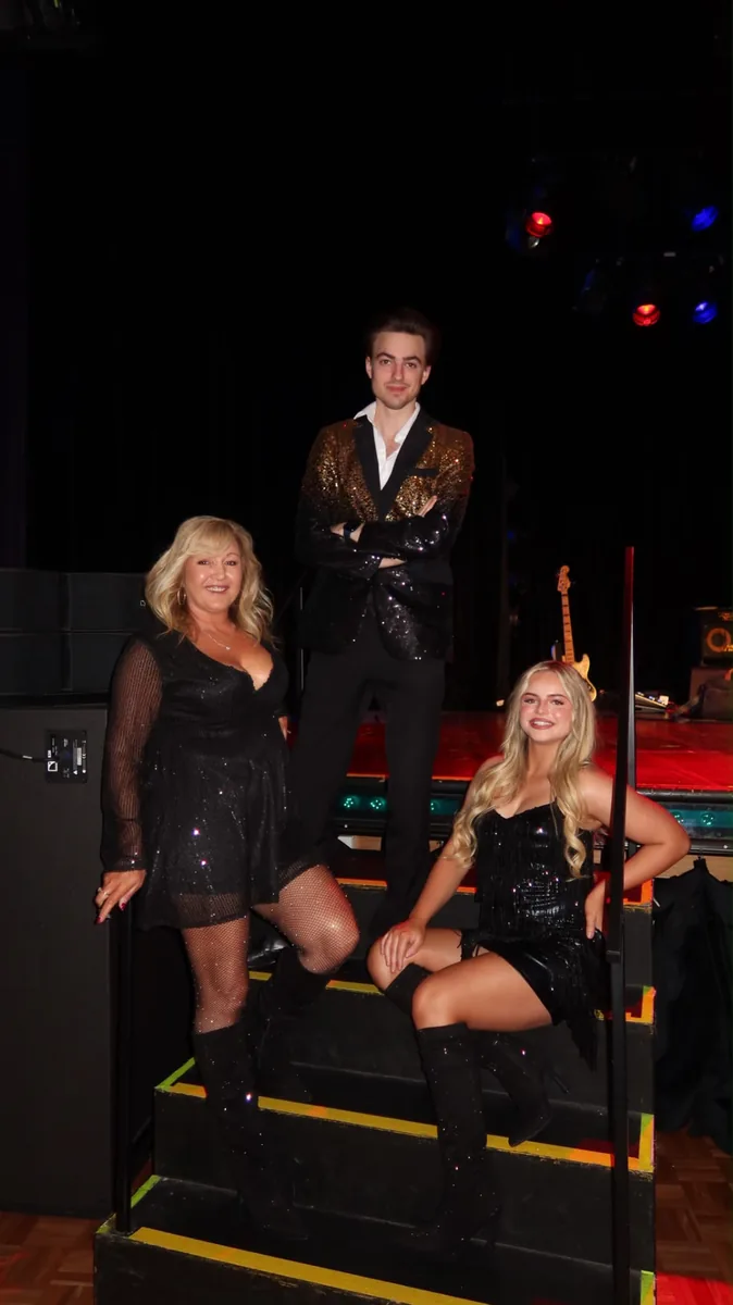 Three singers in sequined outfits posing on backstage steps